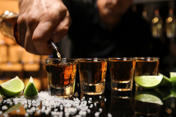 Bartender pouring tasty tequila into glasses at table in bar, closeup