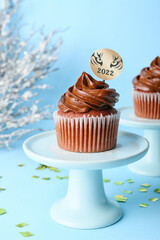 Tasty cupcake for New Year 2022 celebration on color background