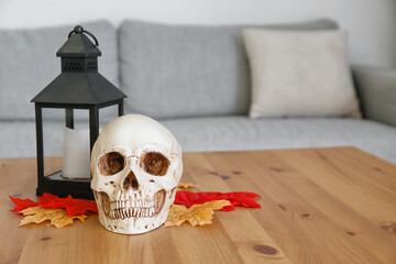 Human skull with candle and fallen leaves on table in room