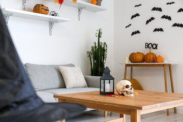 Human skull with candle and fallen leaves on table in room