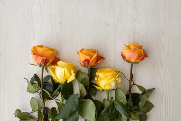 bouquet of yellow roses with orange edge lying neatly on a wooden table, detail of the petals, stem and leaves, nature in studio, backgrounds with natural flowers