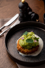 Menu photography in a dark restaurant: roasted fish cake with avocado and garlic sauce on a black dish, soft light