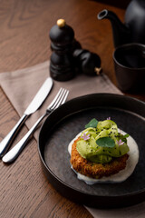 Menu photography in a dark restaurant: roasted fish cake with avocado and garlic sauce on a black dish, soft light
