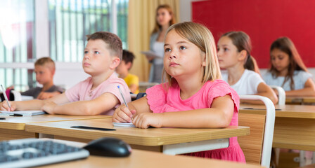Fototapeta premium Pupils sitting in classroom during lesson. Female teacher standing behind.