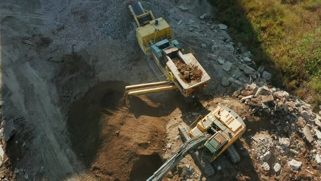 Drone shot from the top down on an excavator loading rocks into a portable rock crusher. Two heavy excavators are working on a construction site they are digging up large rocks and throwing boulders 
