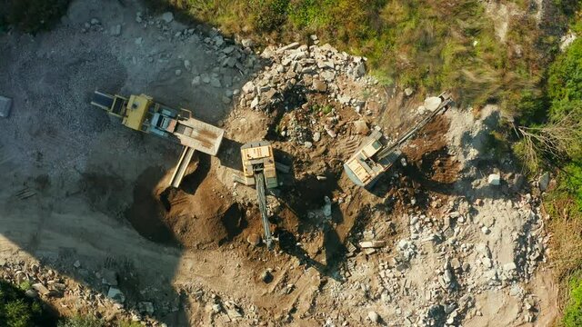 Top view of an excavator loading a stone into a crusher. Heavy mining equipment is working on a construction site, an excavator breaks stones and loads them into a crusher. Mobile stone jaw crusher 