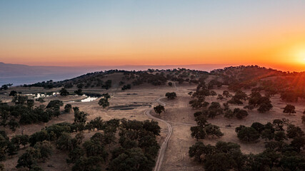 Aerial View of a Valley, Lake and Rolling Hills Covered in Oak Trees and Blanketed in a California Sunset