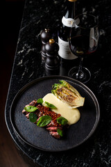 Dark atmospheric photo of raw bloody steak on a black dish with a glass of good red wine