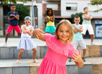 Confident preteen b-girl dancing with group of friends on city street. Urban lifestyle. Hip-hop generation..