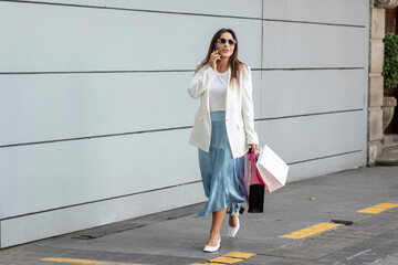 Fototapeta premium Hermosa mujer con bolsas de compras caminando por la calle mientras habla por teléfono