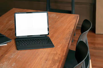 Blank white screen tablet with magic keyboard on wooden table in living room with vintage style.