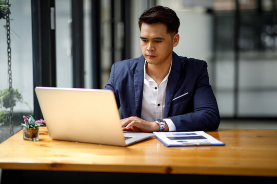 Young handsome man or businessman working on laptop computer in modern office.doing finances,accounting analysis,report,data and pointing graph Freelance education and technology concept.