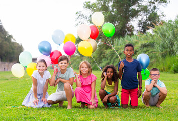 Group of boys and girls playing on field with multicolored balloons.