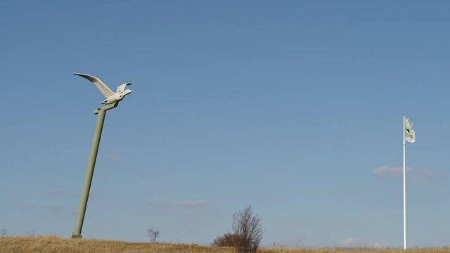 a statue of a bird on a high pillar with a flag blowing in the wind - calm slow shot