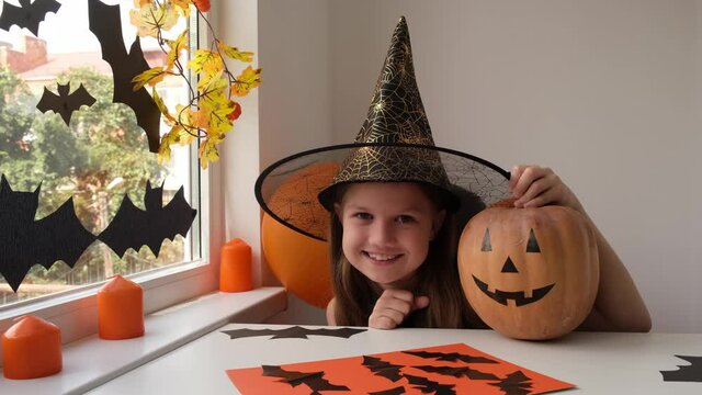 Smiling happy little girl in witch costume preparing for Halloween party at home. Holiday decoration concept