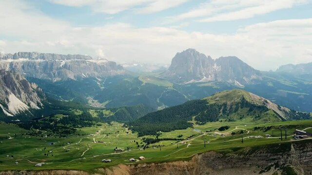 Droneshot of green meadows in the dolomites in northern italy. The drone flies over the mountain ridge and films the green hiking region with typical dolomite mountains in the background.