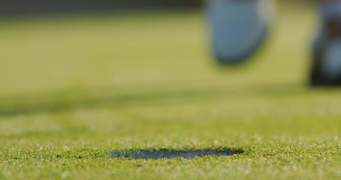  A person feet walking toward a golf hole picking up a golf ball, static shot