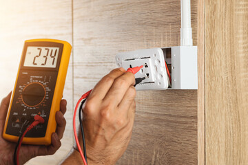 Close up hand of an electrician uses a digital meter to measure the voltage at a wall socket on a...