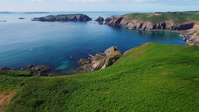Drone flying towards revealing a big isolated house in the middle of a green landscape in the Island of Sark, Channel Islands.