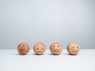 Customer service evaluation, feedback, and satisfaction survey concept. Wooden balls with a cute happy smiling emoticon with another emotional faces on white background with copy space.