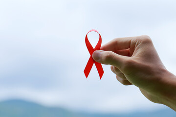 Close up hands holding an aids red ribbon on nature background.healthcare and medicine concept