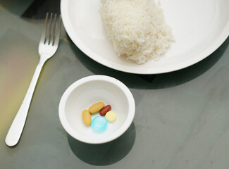 Tablets in a container for medicinal and dietary supplements, on the table, with rice in a plate and a fork.