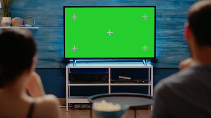 Young adults looking at modern technology green screen on television at home. Caucasian people with copy space and virtual chroma key for isolated template or mockup background - Powered by Adobe