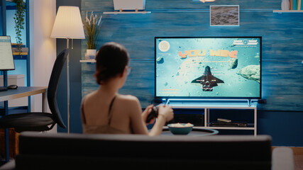 Caucasian woman winning videogames competition of action simulator with console and TV. Young adult holding controller and playing video animation at home for entertainment and fun © DC Studio