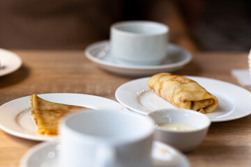 Fresh pancakes with filling on the table next to white mugs for coffee or tea for breakfast. Pancakes for a sweet dessert after lunch in a cozy coffee.