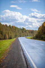 Fototapeta premium Straight road with a marking on the nature background. Open Road in future, no cars, auto on asphalt road through green forest, trees. Clouds on blue sky in summer, sunshine, sunny day. Bottom view