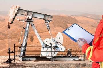 Oil worker in uniform recording maintenance of the pump jack at petrochemical industrial