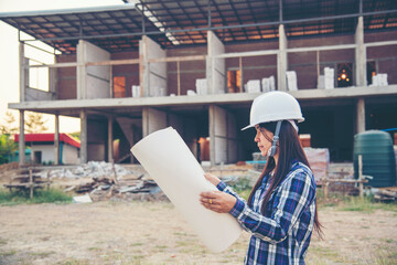 Woman construction engineer hold blueprint wear plaid shirt safety white hard hat at construction site industry labor worker. Architecture Female engineer civil worker look at blueprint real estate