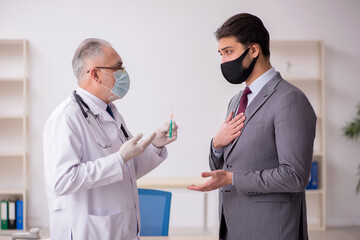 Young businessman visiting old male doctor in vaccination concep