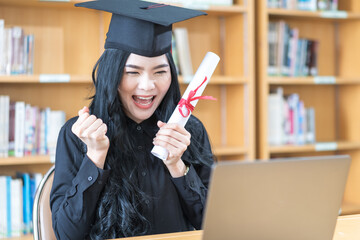 Young Asian university woman graduate in graduation gown and mortarboard with degree certificate celebrates with family through video call on laptop in virtual convocation during COVID-19 pandemic