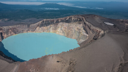 Turquoise acidic lifeless lake in the crater of a volcano. Deposits of sulfur on the surface. On the steep rocky slopes, devoid of vegetation, the shadow of a helicopter. Aerial view. Kamchatka