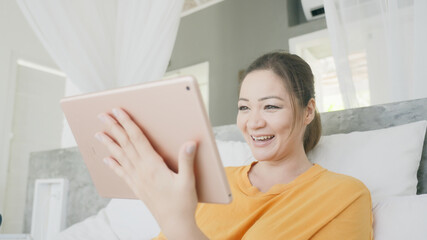 A beautiful mixed-race girl is surprised by a call on a tablet and starts talking via video on a tablet. A successful Woman who is on self-isolation communicates with colleagues sitting in bed. 