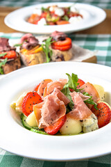 Salad with strawberry, prosciutto, herbs, cottage cheese and blackberry balsamic vinegar arranged on white plate.