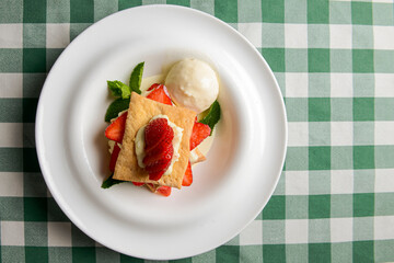 Puff pastries with strawberries and berry sauce on a white plate. Over green plaid background.