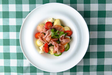 Salad with strawberry, prosciutto, herbs, cottage cheese and blackberry balsamic vinegar arranged on white plate.