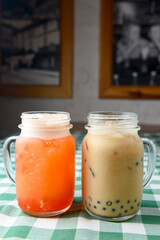 Row of fresh boba bubble tea glasses on wooden table with green plaid tablecloth background.