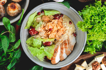 Fresh salad with chicken breast, cheese and tomatoes. Served in a bowl on a wooden table.