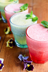 Delicious healthy kiwi and strawbeery, raspberry smoothies served with fresh mint in glasses on rustic wooden table.