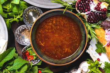 Soup Kharcho with beef meat on a rustic table surrounded by spices, fresh greens and vegetables.