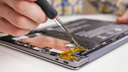 Unrecognizable man disassembles a laptop and looks through the parts with a screwdriver.