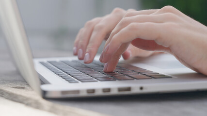 A freelance girl is typing a letter about work on the laptop keyboard. Close-up of a woman's fingers typing on a computer, against the background of a green garden on a sunny day. Work online.
