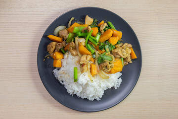 A plate of chicken and vegetable stir-fry with steam rice.
