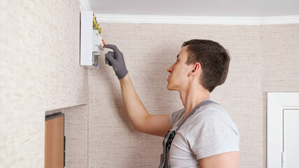 Professional electrician in jumpsuit presses levers on contemporary switchboard to fix above front...