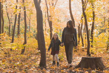 Young woman and her child girl walking through autumn park. Single parent and motherhood concept.