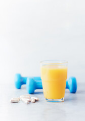 Glass of Orange Juice. Blue Dumbbells and Sport supplements ( Carnitine capsules ) in background. Stone background. Close up.
