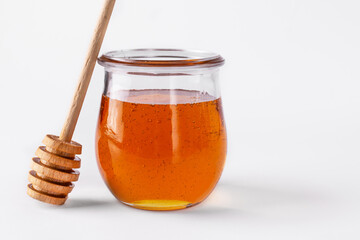 Honey in a glass jar and wooden honey dipper on white background. Honey, as a healthy sweet dessert.